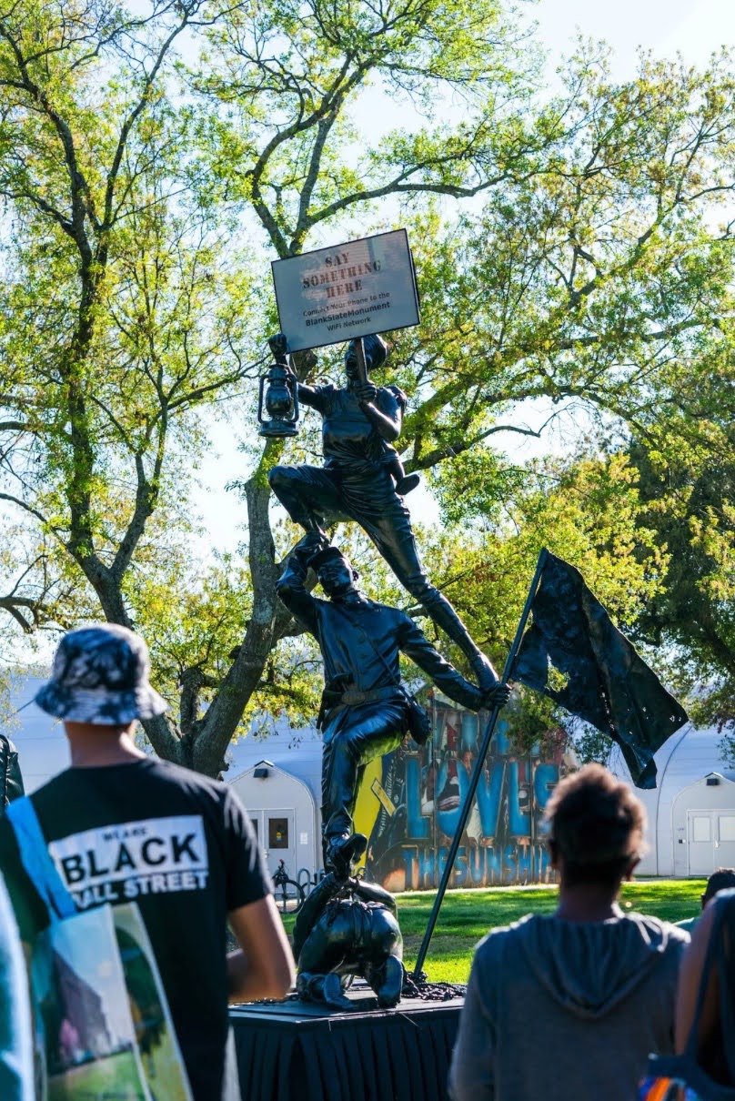 People gather around the Blank Slate Monument at Rice University’s campus in March 2023. The monument’s slate reads: “SAY SOMETHING HERE. Connect Your Phone to the BlankSlateMonument WiFi Network.” Image Credit: Rice University News, Photograph by Gustavo Raskosky.